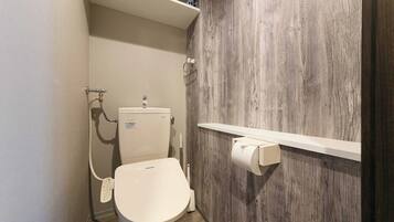 A compact bathroom with a white toilet, a wooden wall, and a shelf above the toilet holding toiletries.
