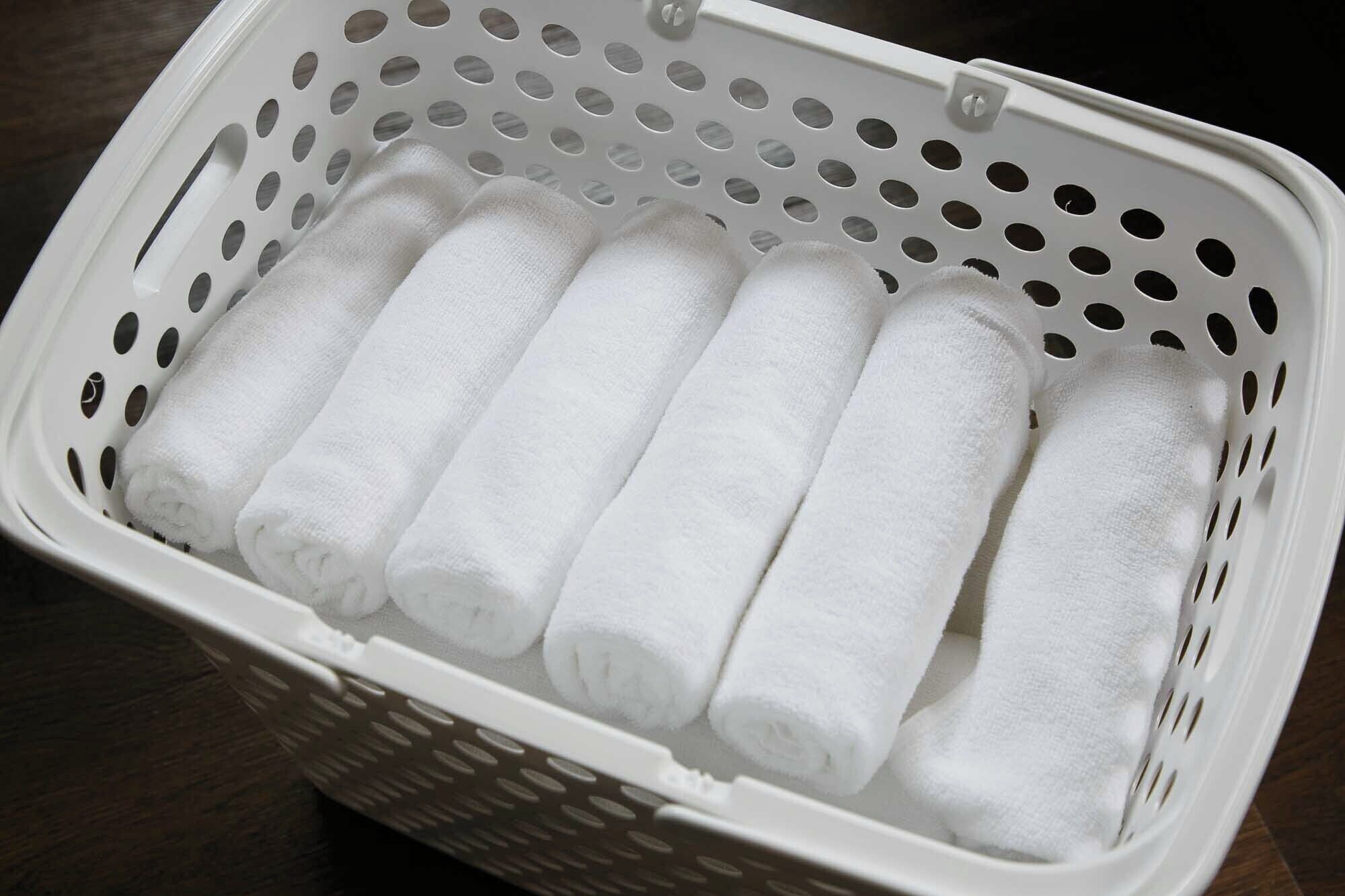 Uma cesta de plástico branca com toalhas brancas dobradas.