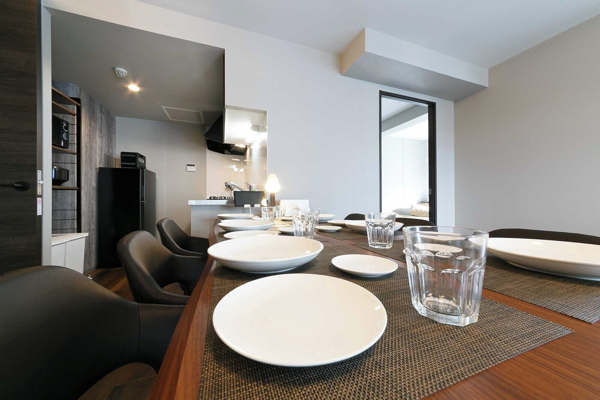 A modern dining area with a long wooden table set for four, equipped with white plates and clear glasses.