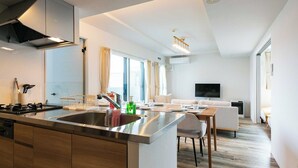 Una cocina moderna con una isla central, un comedor con mesa y sillas, y una sala de estar con sofá y televisor montado en la pared.