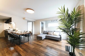 A modern living room with a dining area, a grey sofa, and a large green plant. - Twinberry CHITOSE (Chitose)