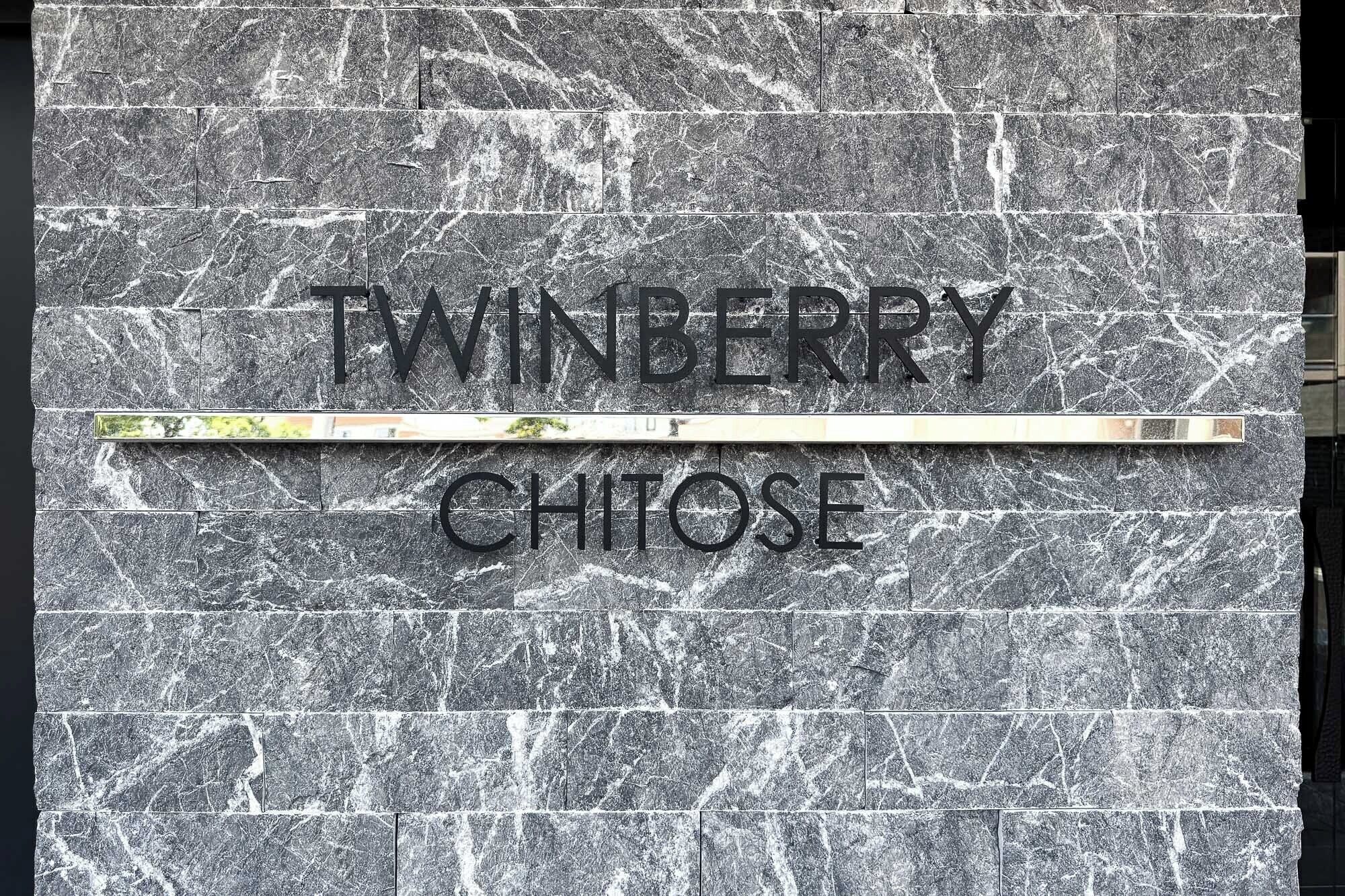 Une enseigne portant le nom « TWINBERRY CHITOSE » est fixée à un mur texturé.