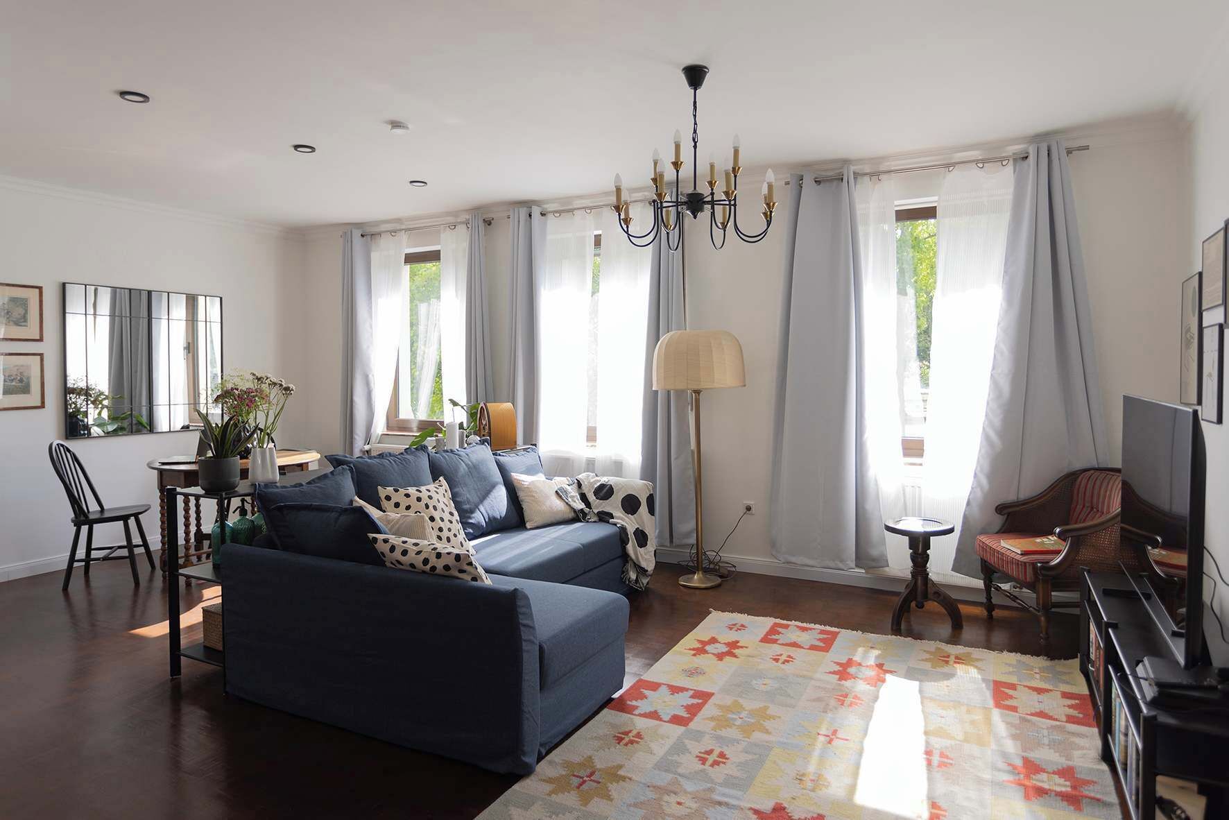 Una sala de estar con un sofá azul oscuro, un tapete estampado, una lámpara de pie y un televisor.