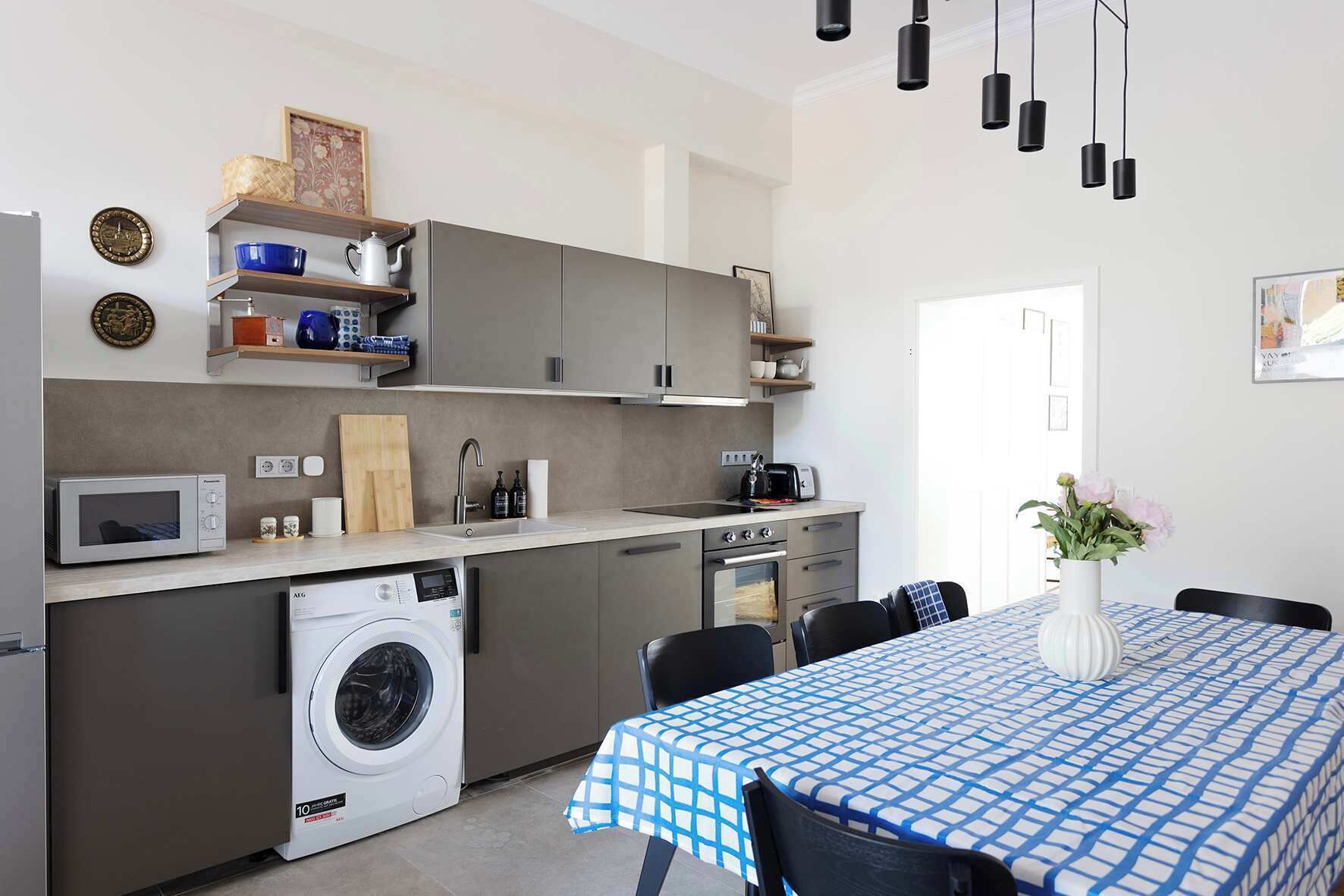 A compact kitchen with a washing machine, microwave, and oven. There is a dining area with a table and chairs.