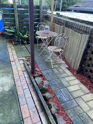 A patio area with a table and chairs, a wooden fence, and a brick wall. - Beach to Bush, is a private one bedroom apartment with off street parking . (Stanwell Park)