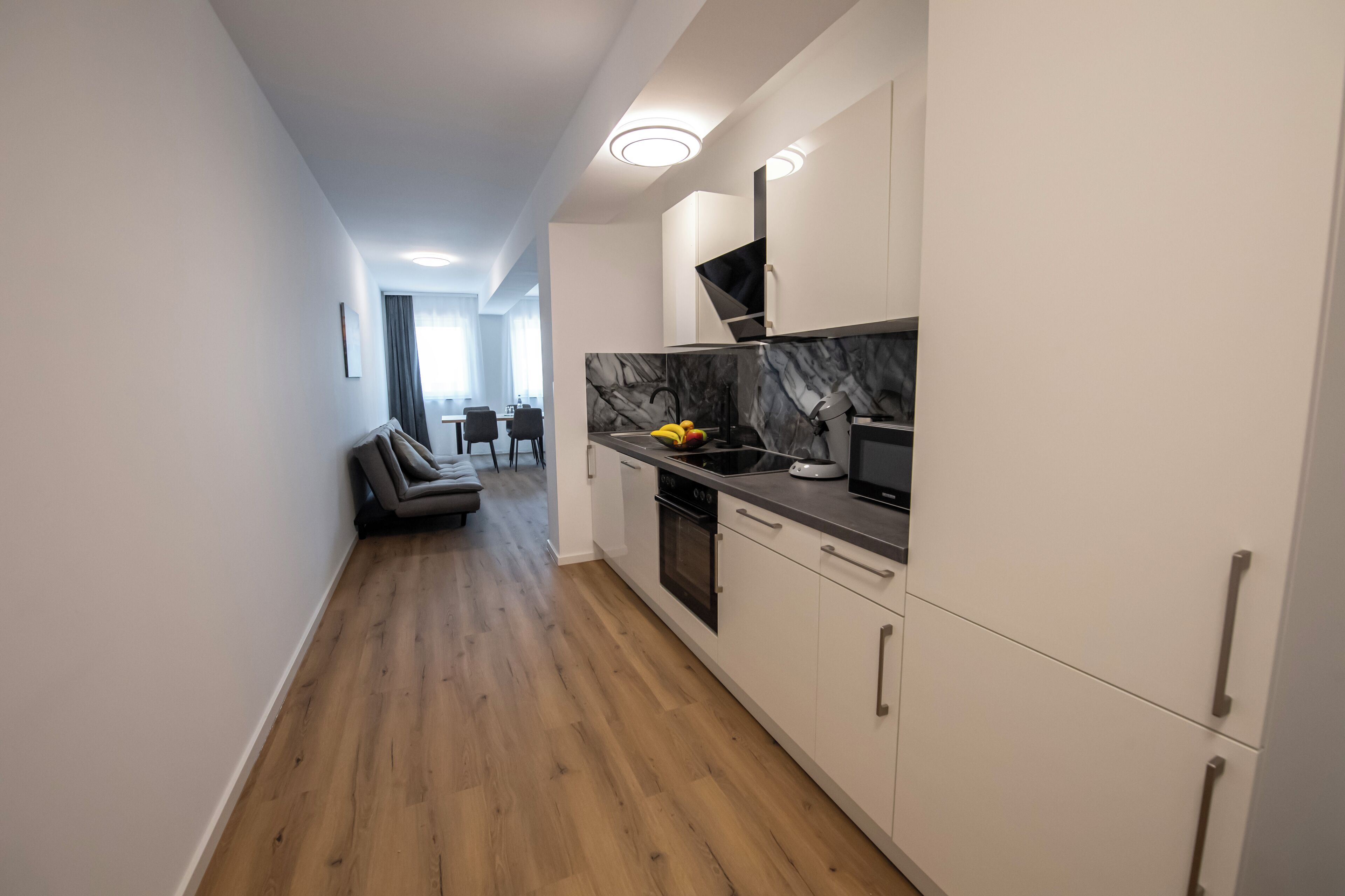 A modern kitchen with white cabinets, a marble countertop, and a built-in oven.