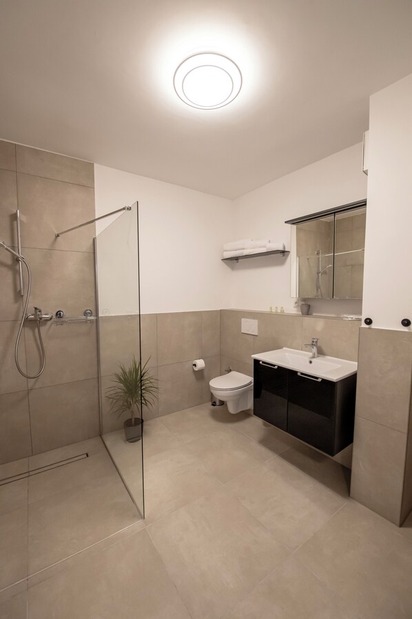 Un baño moderno con cabina de ducha de vidrio, inodoro, lavabo con espejo y una planta en maceta.
