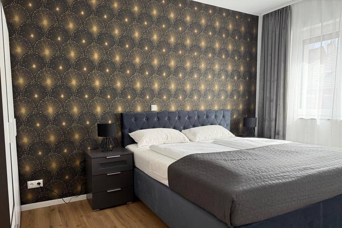Ein Schlafzimmer mit einem dunkelblauen Bett, weißer Bettwäsche, einem Nachttisch mit Lampe und einer Wand mit Sternenmuster.