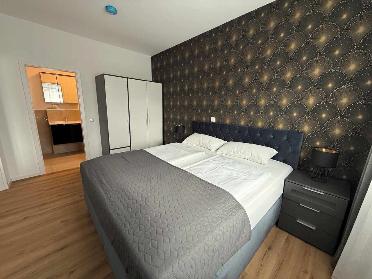 Un dormitorio con cama, mesita de noche, armario y pared con diseño.