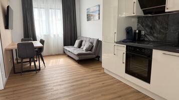 A modern kitchen with white cabinets, a built-in oven, and a dining area with a table and chairs.