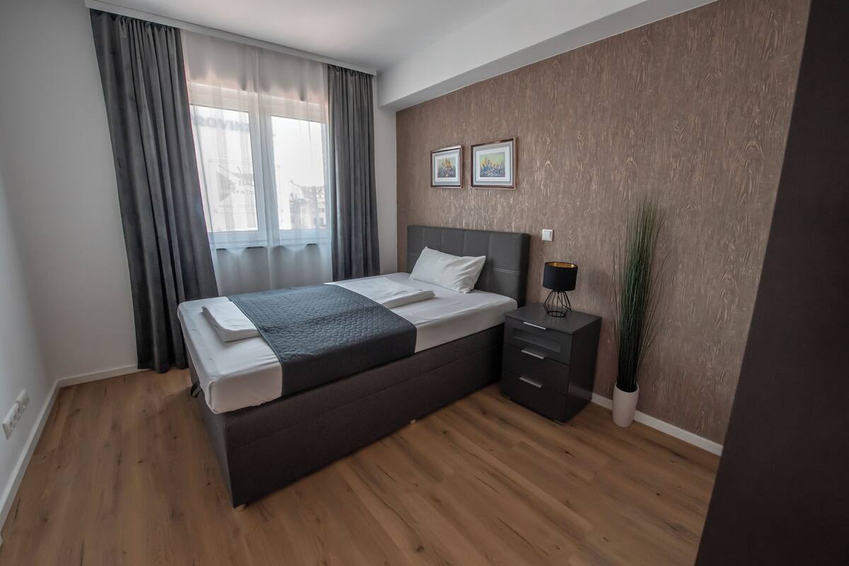 Ein modernes Schlafzimmer mit einem großen Bett, einem Nachttisch, Vorhängen und einem Fenster.