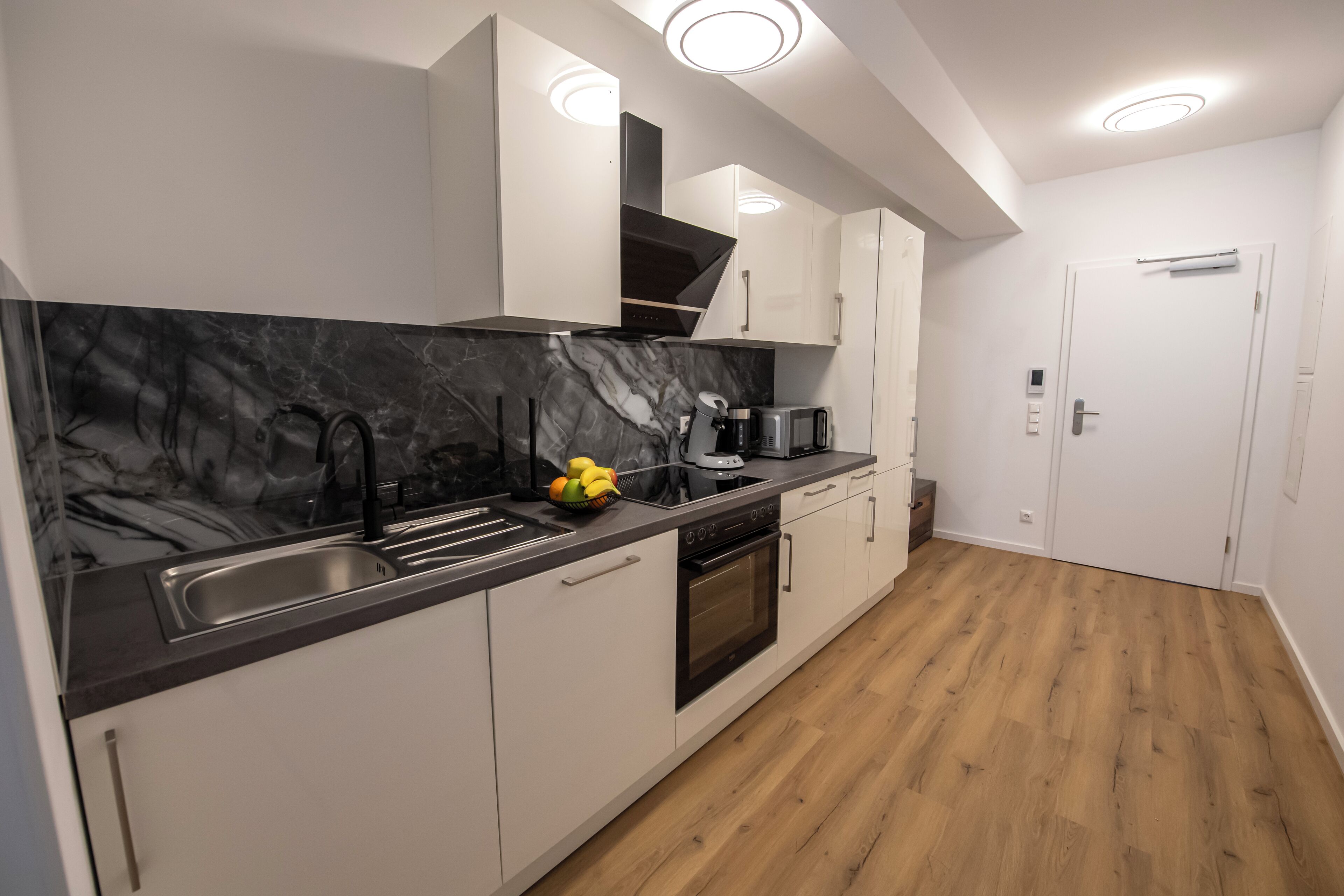 A modern kitchen with a marble countertop, stainless steel sink, and a built-in oven.