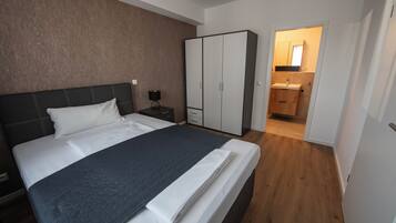 Ein Schlafzimmer mit Bett, Schrank, Nachttisch und einem durch eine offene Tür einsehbaren Badezimmer.