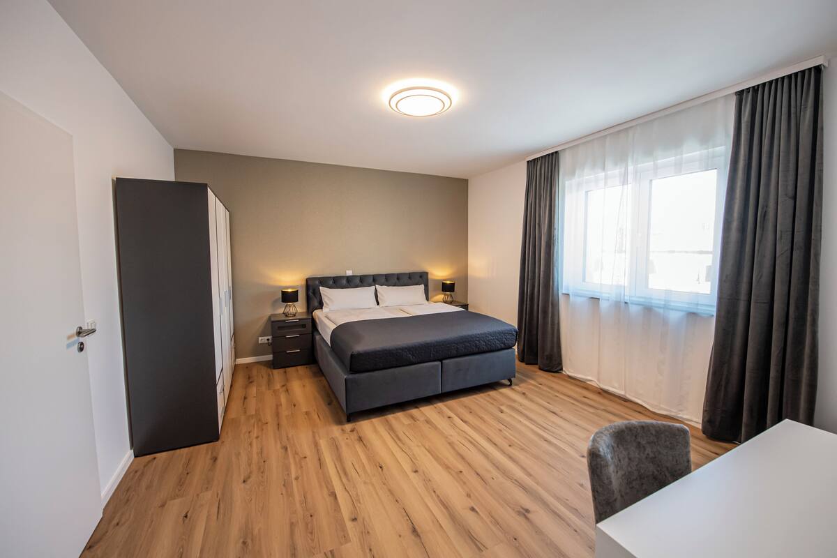 Ein modernes Schlafzimmer mit einem großen Bett, Nachttischen, einem Kleiderschrank und einem Fenster mit Vorhängen.