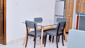 A dining area with a round table and four grey chairs with wooden legs. A white refrigerator is in the background. - Chic 1-bedroom apartment (Accra)