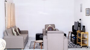 A modern living room with a sofa, armchair, and a TV stand. - Chic 1-bedroom apartment (Accra)