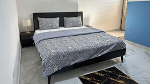 A neatly made bed with patterned bedding, a bedside table with a lamp, and a marble-tiled floor. - Chic 1-bedroom apartment (Accra)
