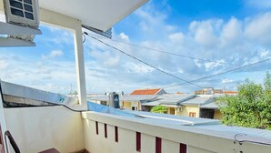 A balcony with two chairs, a table, and a view of neighboring houses.