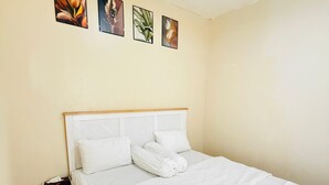 A neatly made bed with white linens and pillows, a wooden nightstand with a tissue box, and a wall with four framed botanical prints.