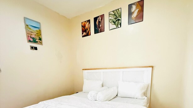 A neatly made bed with white linens in a room with wooden flooring and cream-colored walls.