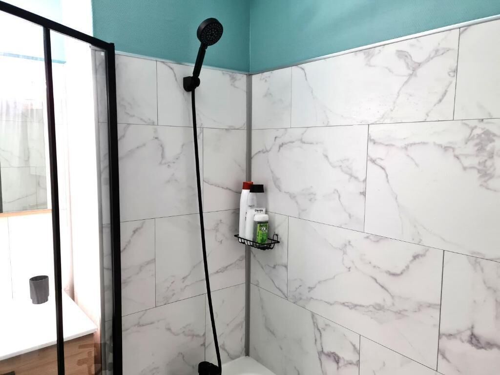 A bathroom with white marble tiles, a showerhead, and a shelf with toiletries.