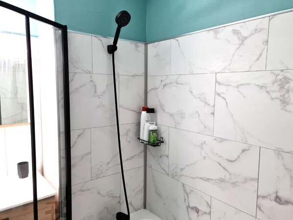 A bathroom with white marble tiles, a showerhead, and a shelf with toiletries.