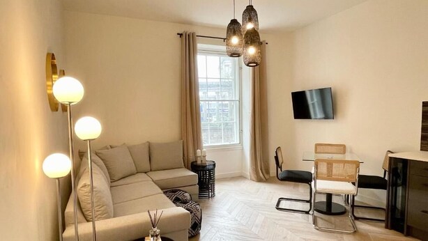 A modern living room with a sofa, a dining table with chairs, a TV mounted on the wall, and a floor lamp. - NEW LISTING Perfect City Location, renovated, comfortable, iconic views (Edinburgh)