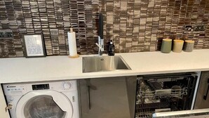 A compact kitchen with a built-in washer and dryer, a stainless steel sink, and a tiled backsplash. - NEW LISTING Perfect City Location, renovated, comfortable, iconic views (Edinburgh)