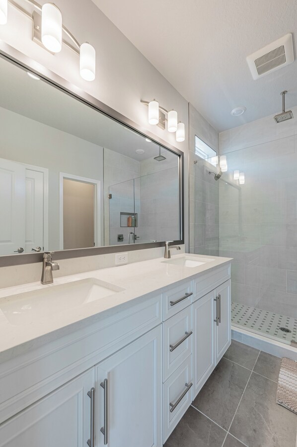 A modern bathroom with a large mirror, dual sinks, and a glass-enclosed shower area.