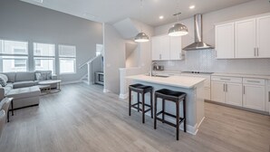A modern kitchen with white cabinets, a large island with stools, and pendant lighting. - All the Florida fun you can have in this charming 3-bedroom townhome in downtow (Sarasota)