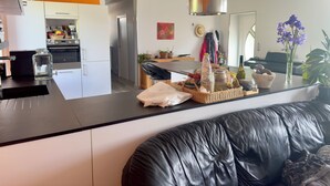 A modern kitchen with white cabinets, an orange accent wall, and a stainless steel refrigerator. - Les Sylphides (Pruzilly)