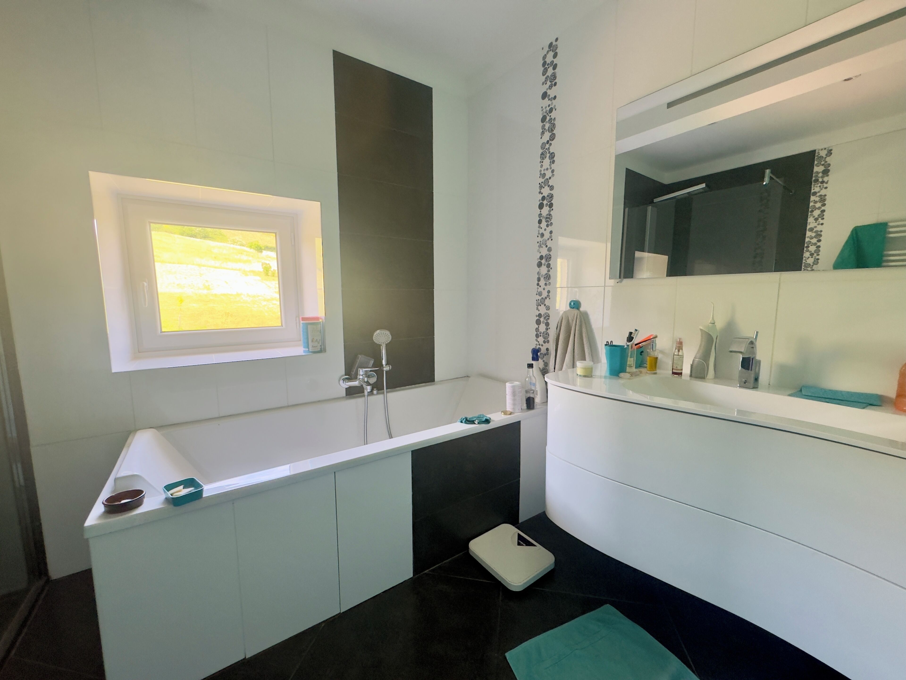 A modern bathroom with a large mirror, a window, a shower, and a scale.