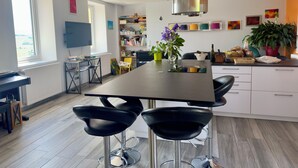 A modern kitchen with a central island, black bar stools, a dining table, and a variety of decorative items. - Les Sylphides (Pruzilly)