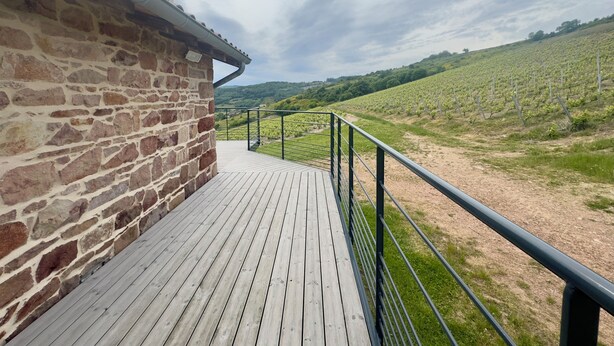 A stone building with a wooden deck and a metal railing. - Les Sylphides (Pruzilly)