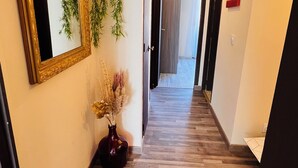 A hallway with a wooden floor, a large mirror, a potted plant, and a vase with dried flowers. - Apartment with 2 large bedrooms (Montpellier)