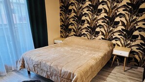 A bedroom with a bed, a nightstand, a lamp, a patterned wallpaper, and a window with curtains. - Apartment with 2 large bedrooms (Montpellier)