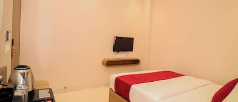 A hotel room with a bed, a TV mounted on the wall, a coffee maker, and a small table with a kettle and cups.