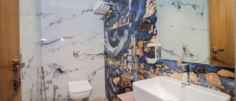 A bathroom with a marble wall, a toilet, a sink, and a shower.