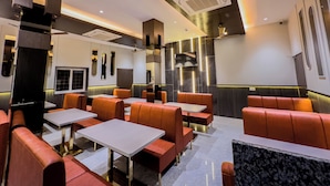 Ein modernes Restaurantambiente mit Sitzbänken und Tischen, Deckenventilatoren, eingelassener Beleuchtung und einem an der Wand befestigten Flachbildfernseher.