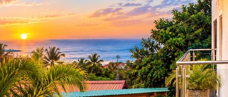 A patio with a sofa, table, and potted plants, overlooking a beach at sunset.