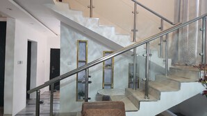 Una escalera moderna con barandillas de vidrio y pasamanos metálico, que lleva a un descansillo con una mesa y sillas de vidrio.