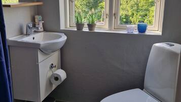 Une salle de bain équipée de toilettes, d’un lavabo et d’une fenêtre donnant sur un espace verdoyant.