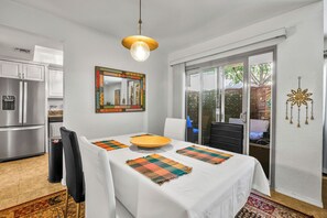 Une cuisine moderne dotée d’appareils électroménagers en acier inoxydable, un coin repas avec une table blanche et des sets de table colorés, et un grand miroir avec un cadre décoratif.