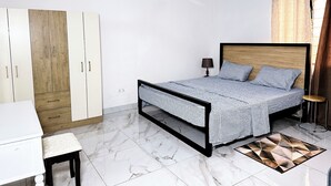 A bedroom with a bed, a desk, a wardrobe, and an air conditioning unit.