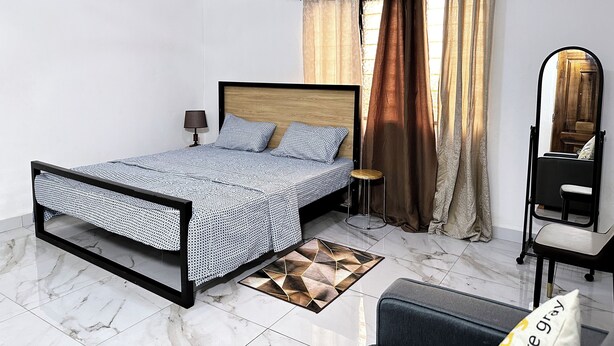 A bedroom with a bed, a nightstand, a lamp, a mirror, and a window with curtains.