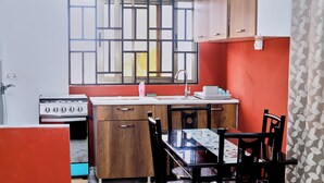 A compact kitchen with a gas stove, wooden cabinets, a dining table with chairs, and a window with bars.