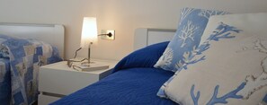 Ein Schlafzimmer mit einem Bett, einem Nachttisch, einer Lampe und einem an der Wand befestigten Lichtschalter.