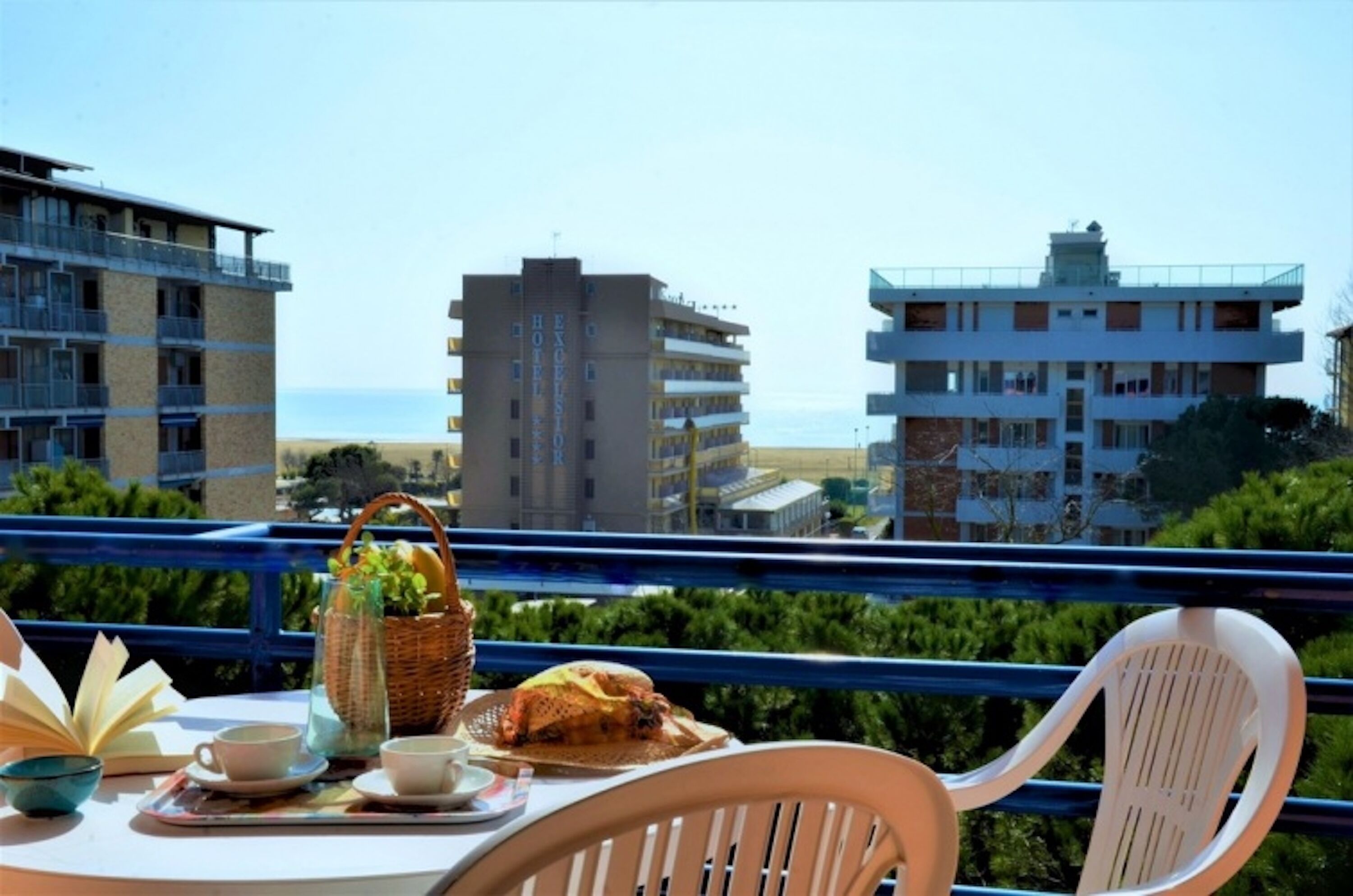 Un balcón con una mesa lista para el desayuno, con vistas a la playa y edificios.
