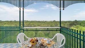 A balcony with a table set for breakfast, overlooking a lush green landscape.