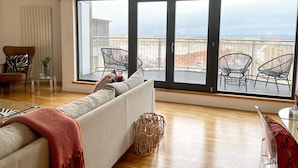 A modern living room with a large sliding glass door leading to a balcony with outdoor furniture.